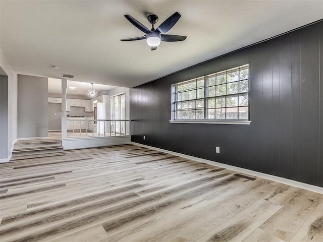 unfurnished living room featuring wood walls, ceiling fan with notable chandelier, and light hardwood / wood-style floors