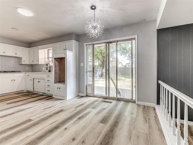 kitchen with backsplash, stainless steel gas cooktop, light hardwood / wood-style flooring, white cabinetry, and hanging light fixtures