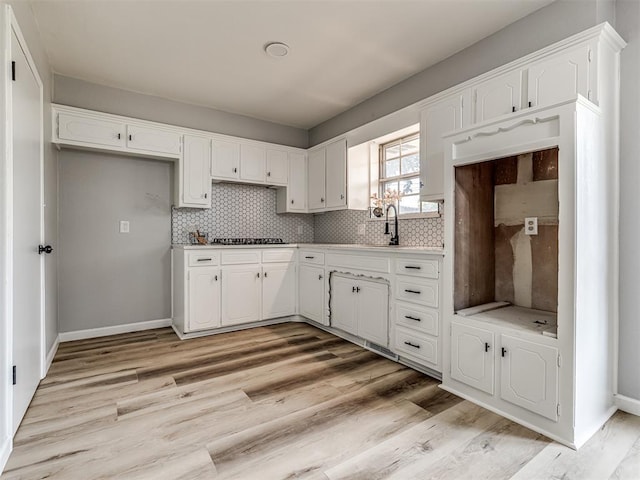 kitchen featuring tasteful backsplash, stainless steel gas cooktop, sink, light hardwood / wood-style flooring, and white cabinets