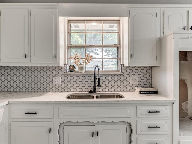 kitchen featuring white cabinets, backsplash, light stone counters, and sink