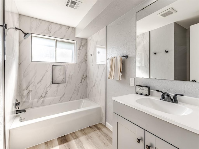 bathroom with wood-type flooring, vanity, and tiled shower / bath