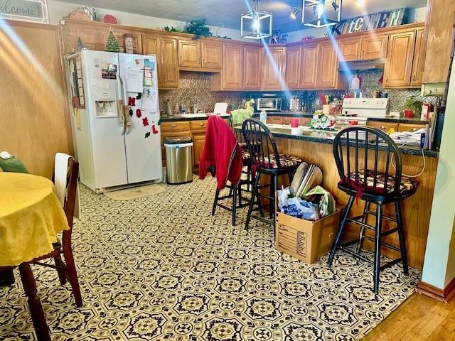 kitchen featuring backsplash, light hardwood / wood-style flooring, white fridge with ice dispenser, a kitchen bar, and range