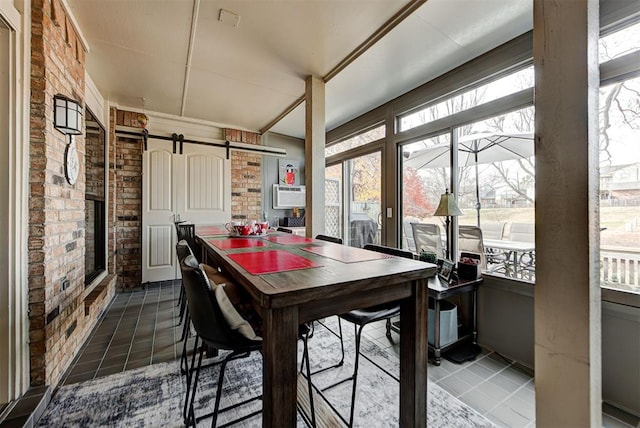 dining space with brick wall, a barn door, dark tile patterned floors, and a sunroom