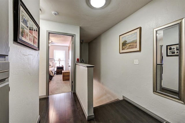 corridor featuring baseboards, dark wood-style flooring, and a textured wall