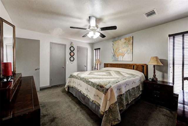 bedroom with multiple closets, dark colored carpet, visible vents, and ceiling fan