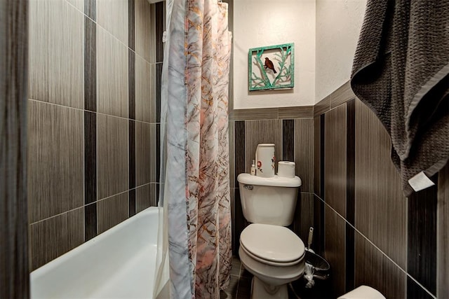 bathroom featuring shower / bathtub combination with curtain, a wainscoted wall, tile walls, and toilet