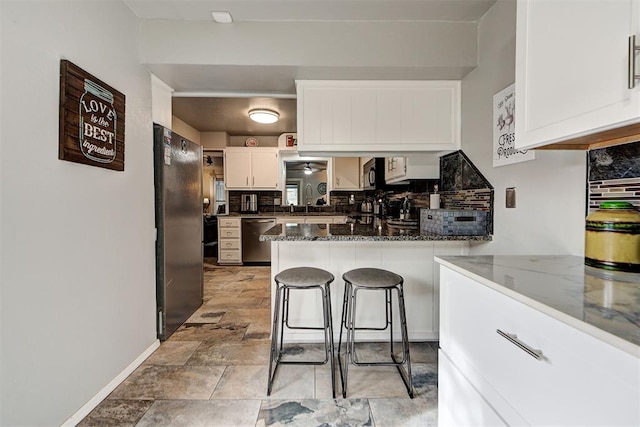 kitchen with a peninsula, a sink, white cabinetry, appliances with stainless steel finishes, and tasteful backsplash