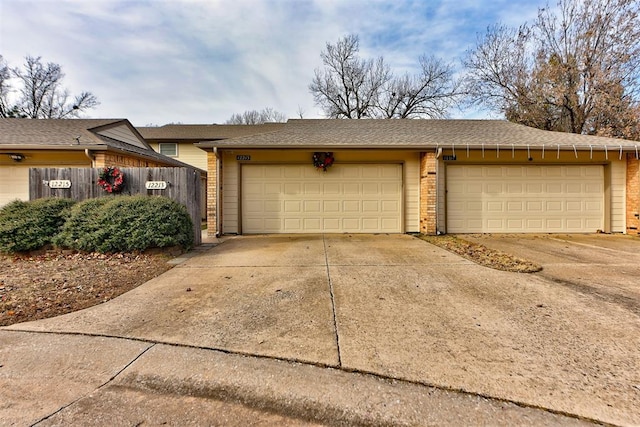 exterior space with a shingled roof, concrete driveway, brick siding, and fence