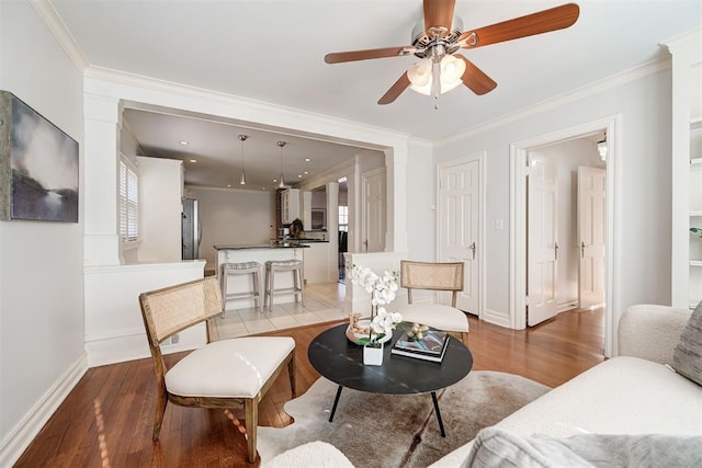 living room featuring light wood finished floors, ceiling fan, baseboards, and ornamental molding