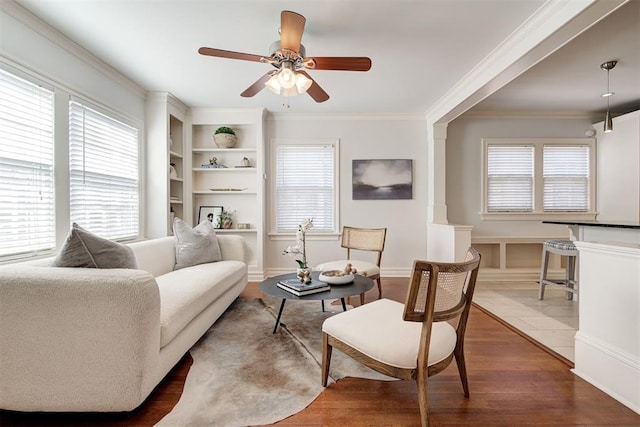 living area with a wealth of natural light, wood finished floors, baseboards, and ornamental molding