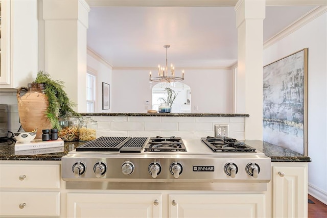 kitchen with ornamental molding, tasteful backsplash, dark stone counters, stainless steel gas stovetop, and white cabinets