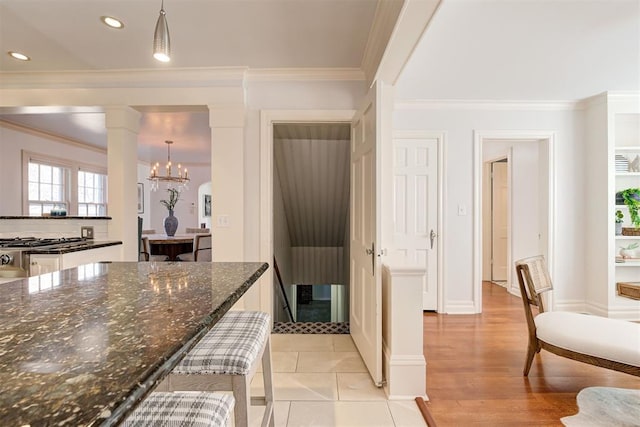 kitchen featuring dark stone countertops, ornate columns, an inviting chandelier, recessed lighting, and ornamental molding