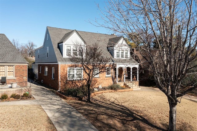 view of front of house featuring brick siding, roof with shingles, and covered porch