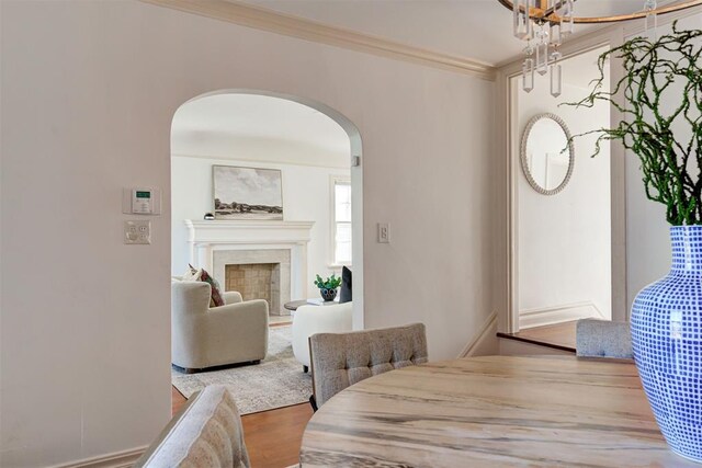 dining room featuring wood finished floors, arched walkways, ornamental molding, and a fireplace