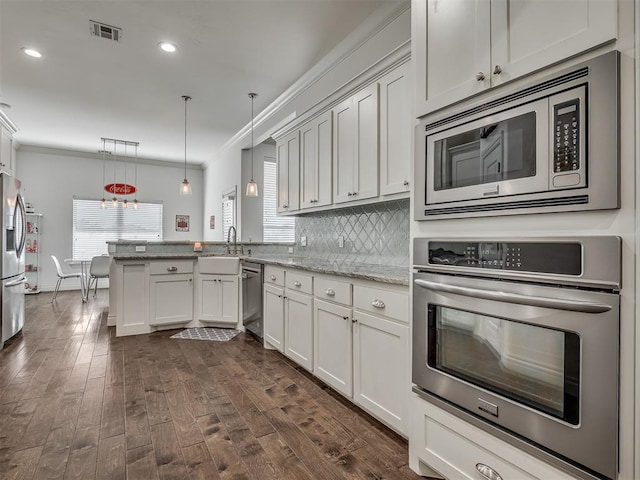 kitchen with tasteful backsplash, light stone counters, ornamental molding, stainless steel appliances, and hanging light fixtures