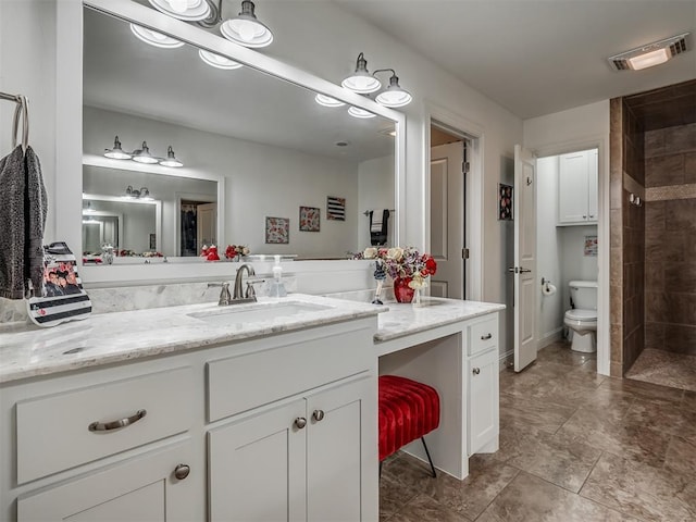 bathroom with a tile shower, vanity, and toilet