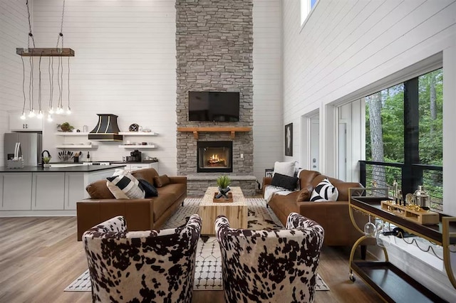 living room with a healthy amount of sunlight, a towering ceiling, a fireplace, and light hardwood / wood-style flooring