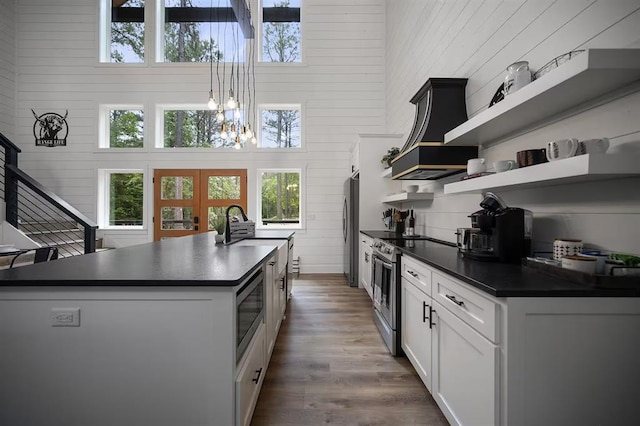 kitchen with appliances with stainless steel finishes, a towering ceiling, a kitchen island with sink, white cabinetry, and wood walls