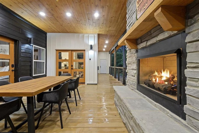 dining room featuring wood walls, an outdoor stone fireplace, light hardwood / wood-style floors, and wood ceiling