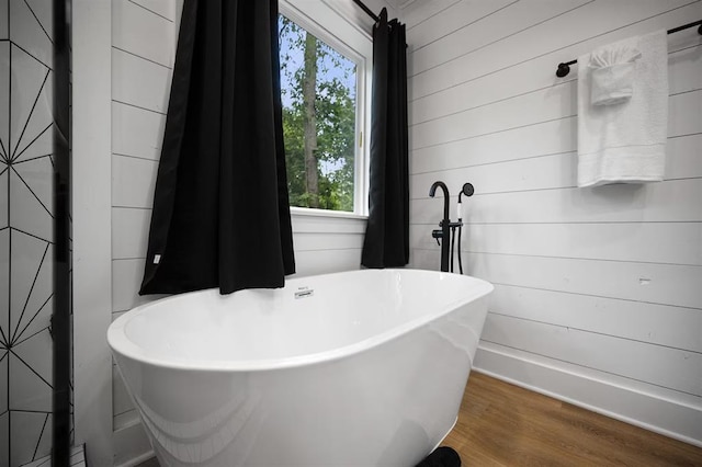 bathroom featuring hardwood / wood-style flooring, wood walls, and a bath