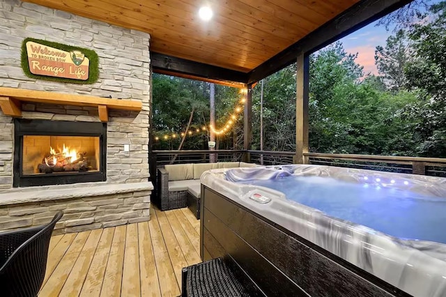 deck at dusk with an outdoor stone fireplace, a grill, and a hot tub