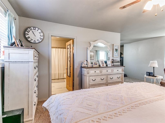 bedroom with ceiling fan, light colored carpet, and ensuite bath