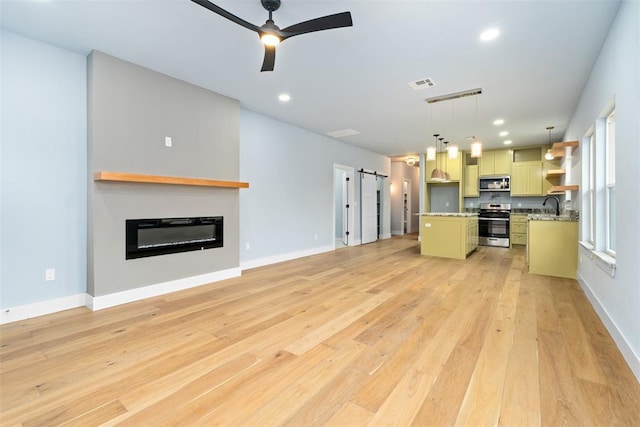 unfurnished living room with a barn door, light hardwood / wood-style flooring, ceiling fan, and sink