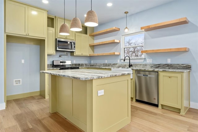 kitchen with light hardwood / wood-style flooring, appliances with stainless steel finishes, decorative light fixtures, a kitchen island, and light stone counters