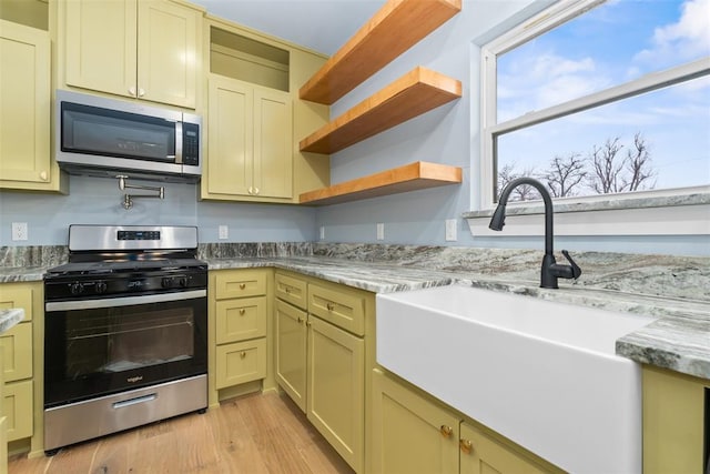 kitchen with light stone countertops, sink, light hardwood / wood-style floors, and appliances with stainless steel finishes