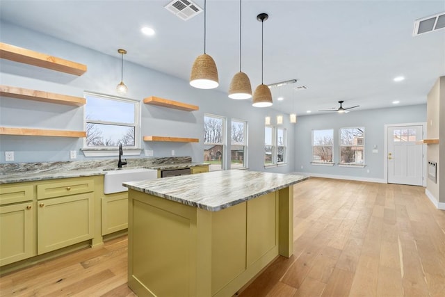 kitchen with light wood-type flooring, light stone counters, ceiling fan, sink, and a center island