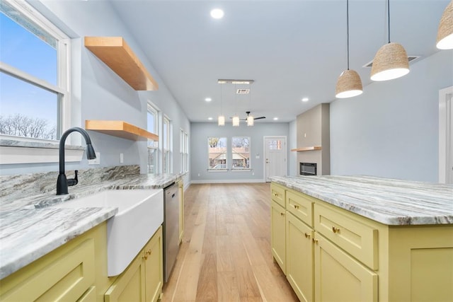 kitchen featuring light stone countertops, dishwasher, sink, cream cabinetry, and a kitchen island