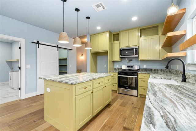 kitchen with a center island, a barn door, light stone counters, and stainless steel appliances