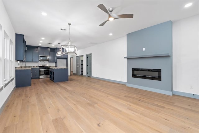 kitchen featuring appliances with stainless steel finishes, a kitchen breakfast bar, ceiling fan with notable chandelier, decorative light fixtures, and a kitchen island