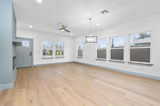 unfurnished living room with a wealth of natural light, light hardwood / wood-style flooring, and ceiling fan with notable chandelier