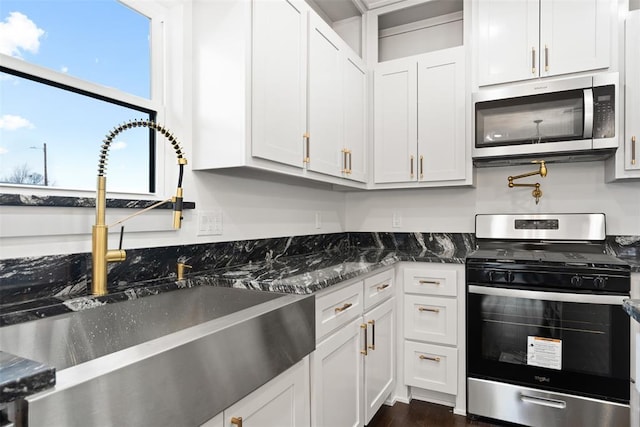 kitchen featuring appliances with stainless steel finishes, white cabinetry, dark stone counters, and sink