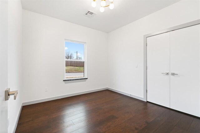 unfurnished bedroom featuring dark hardwood / wood-style flooring, a closet, and a chandelier