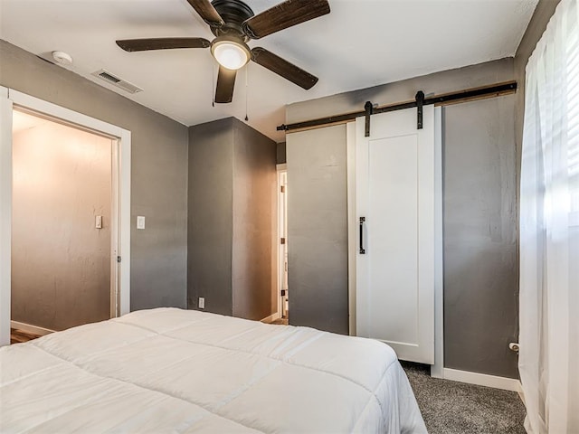 carpeted bedroom with a barn door and ceiling fan