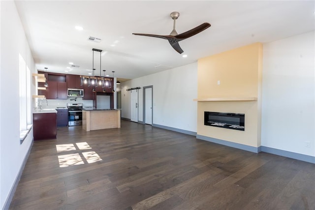 kitchen featuring ceiling fan, a barn door, dark hardwood / wood-style floors, a kitchen island, and stainless steel appliances