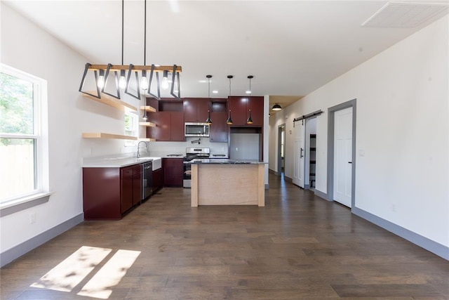 kitchen featuring sink, stainless steel appliances, a barn door, decorative light fixtures, and a kitchen island