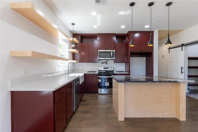 kitchen with dark wood-type flooring, sink, a barn door, appliances with stainless steel finishes, and decorative light fixtures