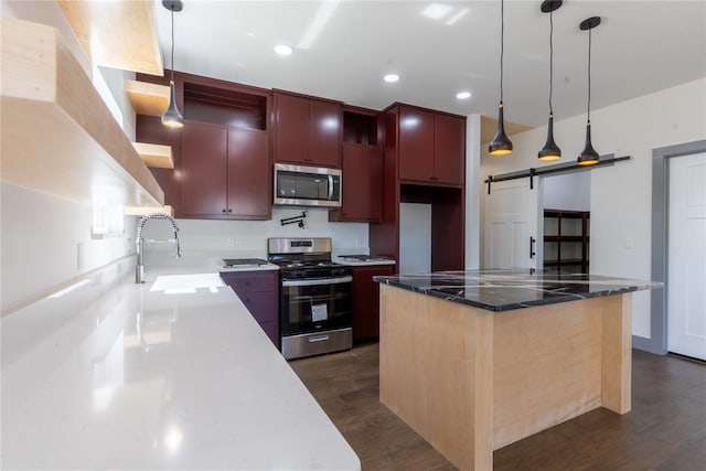 kitchen featuring sink, a barn door, dark stone countertops, a kitchen island, and appliances with stainless steel finishes