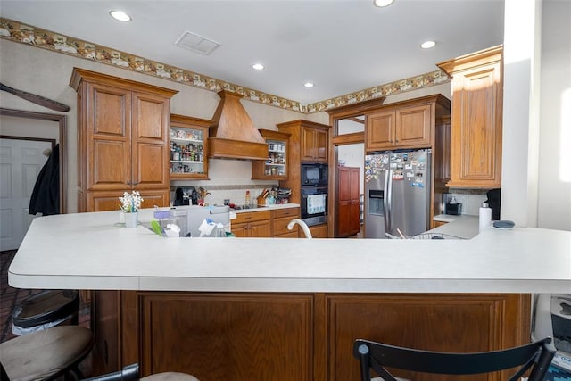 kitchen with premium range hood, black appliances, decorative backsplash, a kitchen bar, and kitchen peninsula