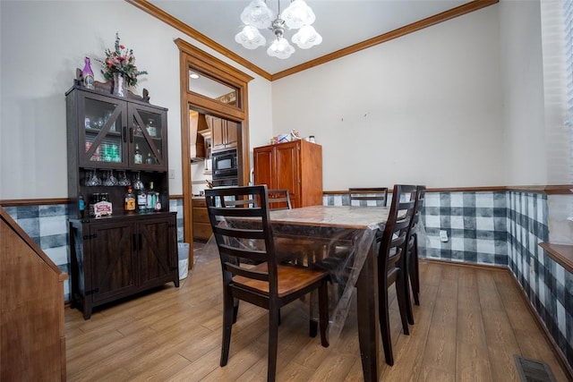 dining space featuring light hardwood / wood-style floors, crown molding, and an inviting chandelier