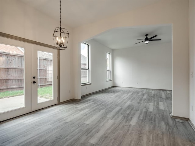 unfurnished dining area with french doors, ceiling fan with notable chandelier, light hardwood / wood-style floors, and a healthy amount of sunlight