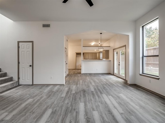 unfurnished living room featuring ceiling fan with notable chandelier, light wood-type flooring, and french doors