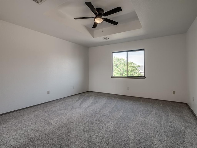 carpeted spare room featuring ceiling fan and a raised ceiling