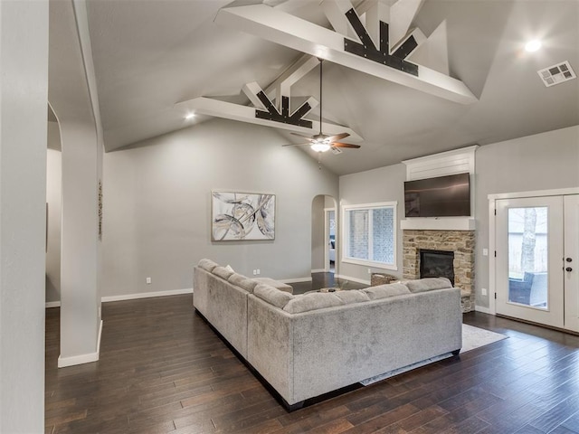 living room with vaulted ceiling with beams, a stone fireplace, ceiling fan, and dark wood-type flooring