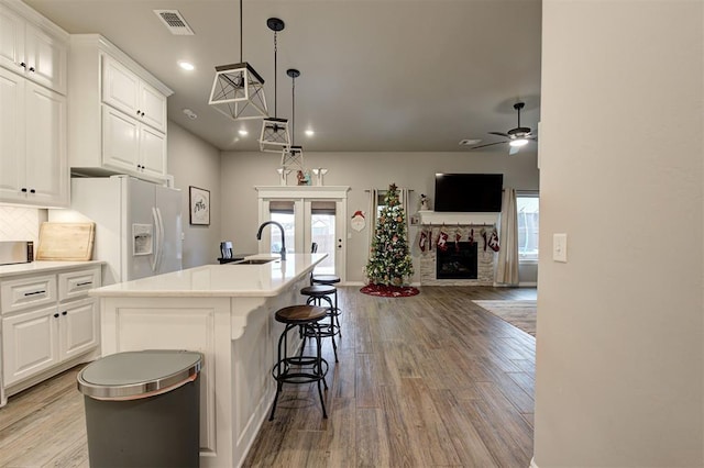 kitchen with a stone fireplace, ceiling fan, a center island with sink, and white cabinets