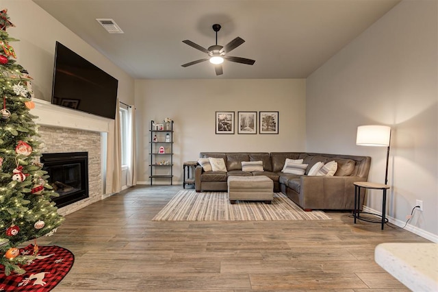 living room featuring a stone fireplace, ceiling fan, and wood-type flooring