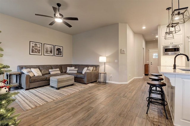 living room featuring ceiling fan, sink, and light wood-type flooring